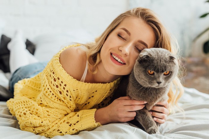 ベッドで女性に抱きつかれて嫌そうな顔をする猫