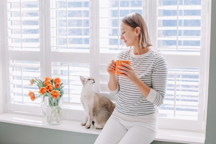 猫と見つめあう、オレンジのコップを持つ女性