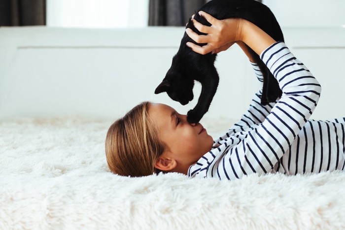寝転ぶ女の子に抱き上げられる黒猫
