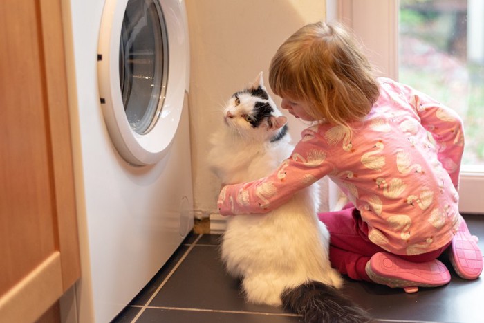 洗濯機の前に座る女の子と猫