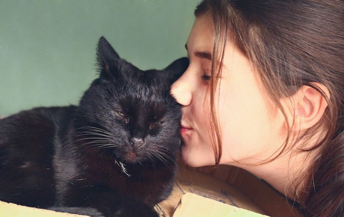 目を閉じた黒猫にキスをする女性