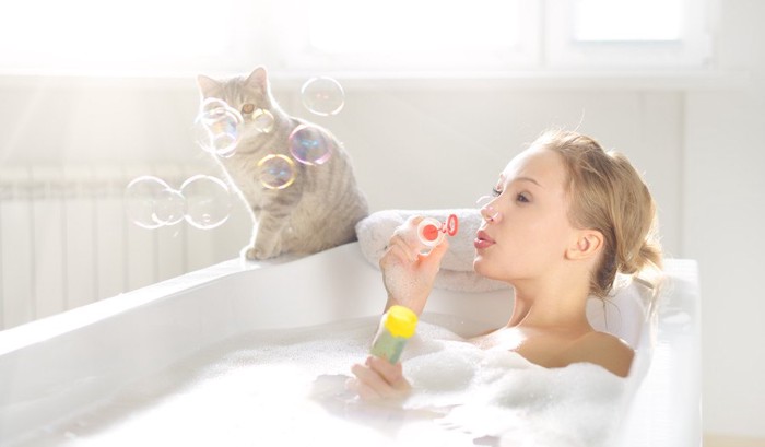 お風呂の縁にいる猫と入浴の女性