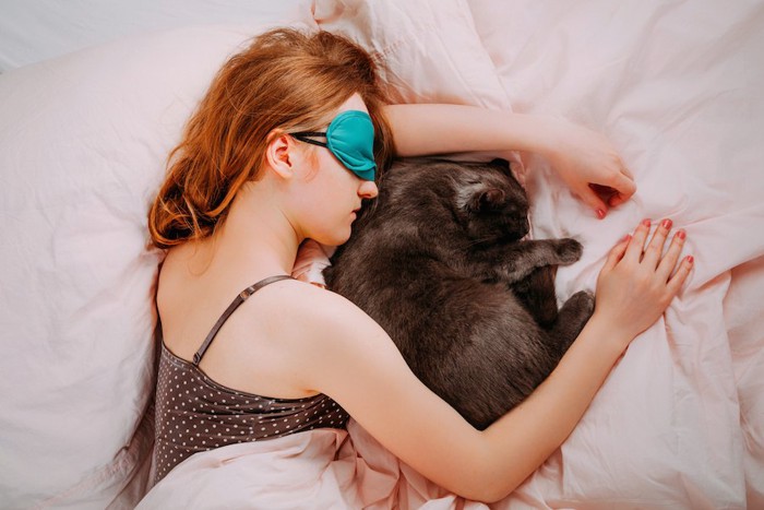 アイマスクをして眠る女性と一緒に眠る猫