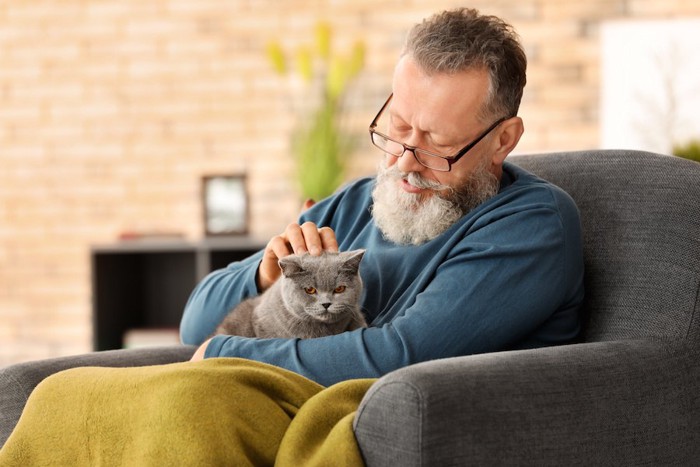 ソファーに座って膝に猫を載せている男性