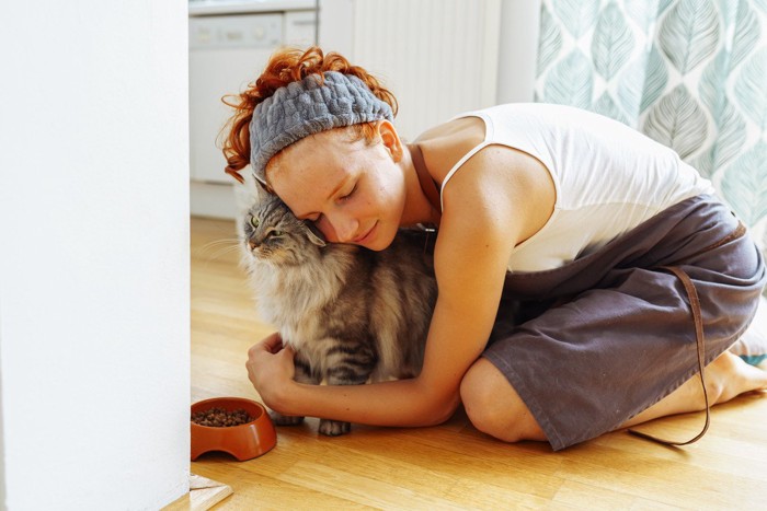 餌を食べようとする猫を抱きしめる女性