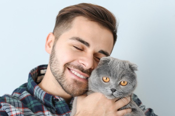 目を閉じて猫を抱きしめる男性と不機嫌そうな顔の猫