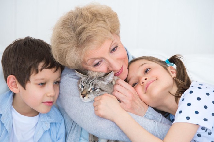 猫を抱きしめる年配の女性と寄り沿う二人の子供