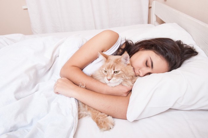 ベッドで猫を抱きしめて眠る女性