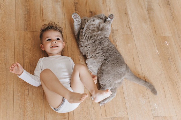 同じ格好で床の上に寝転ぶ猫と子供