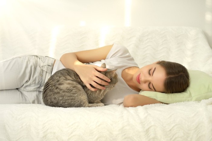 ソファーに横になって猫を撫でる女の子