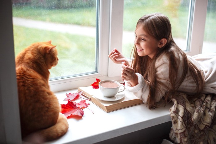 窓辺でココアを飲む少女と猫