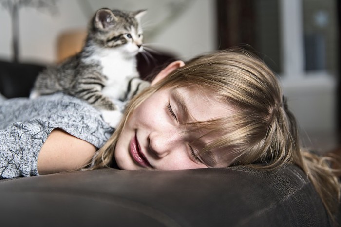 うつ伏せで眠る女性の背中に乗る子猫