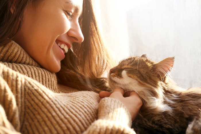 目をつむっている猫にほほえむ女性