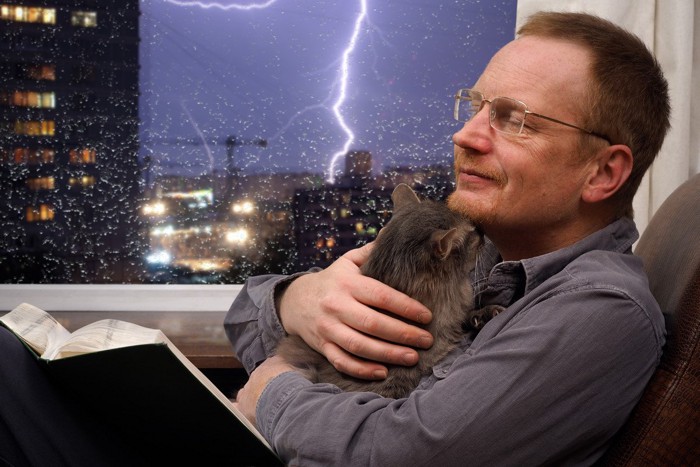 猫を抱いている男性と雷が落ちている風景