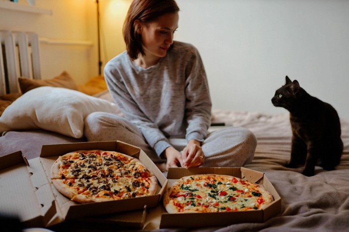 ピザを囲む女性と黒猫