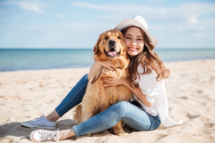 浜辺で笑顔でハグする女性と犬