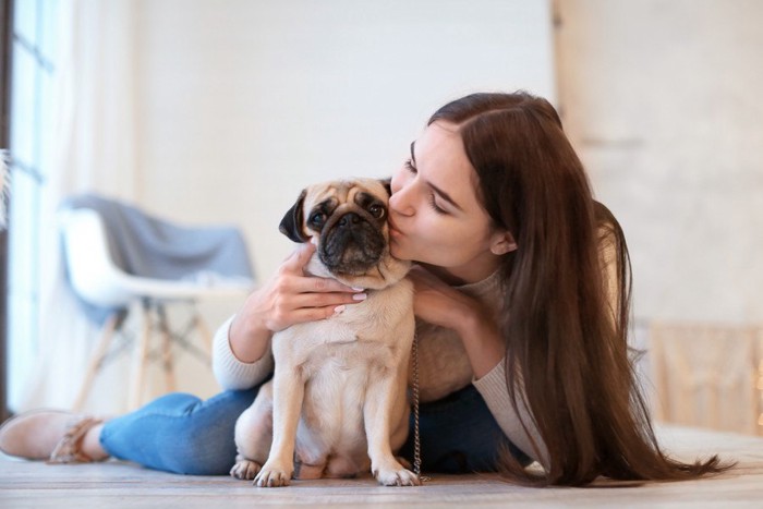 女性にキスをされるパグ