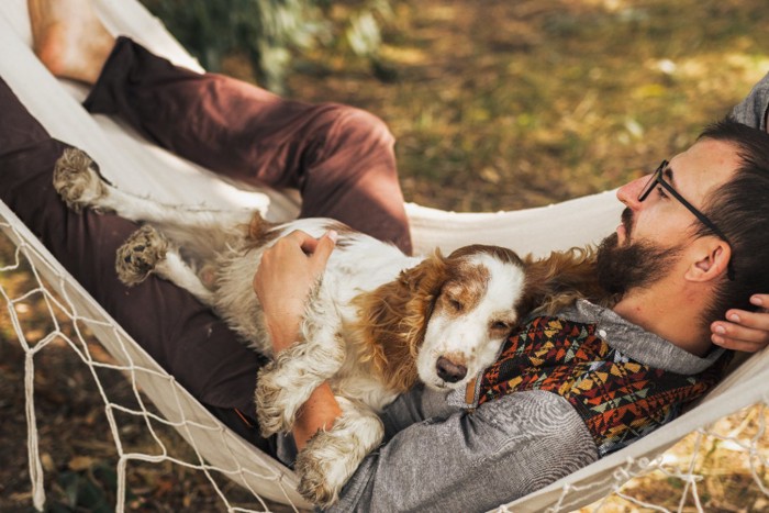 ハンモックに乗る男性とお腹の上で眠る犬