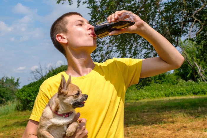 愛犬を抱きながら炭酸飲料を飲む男性